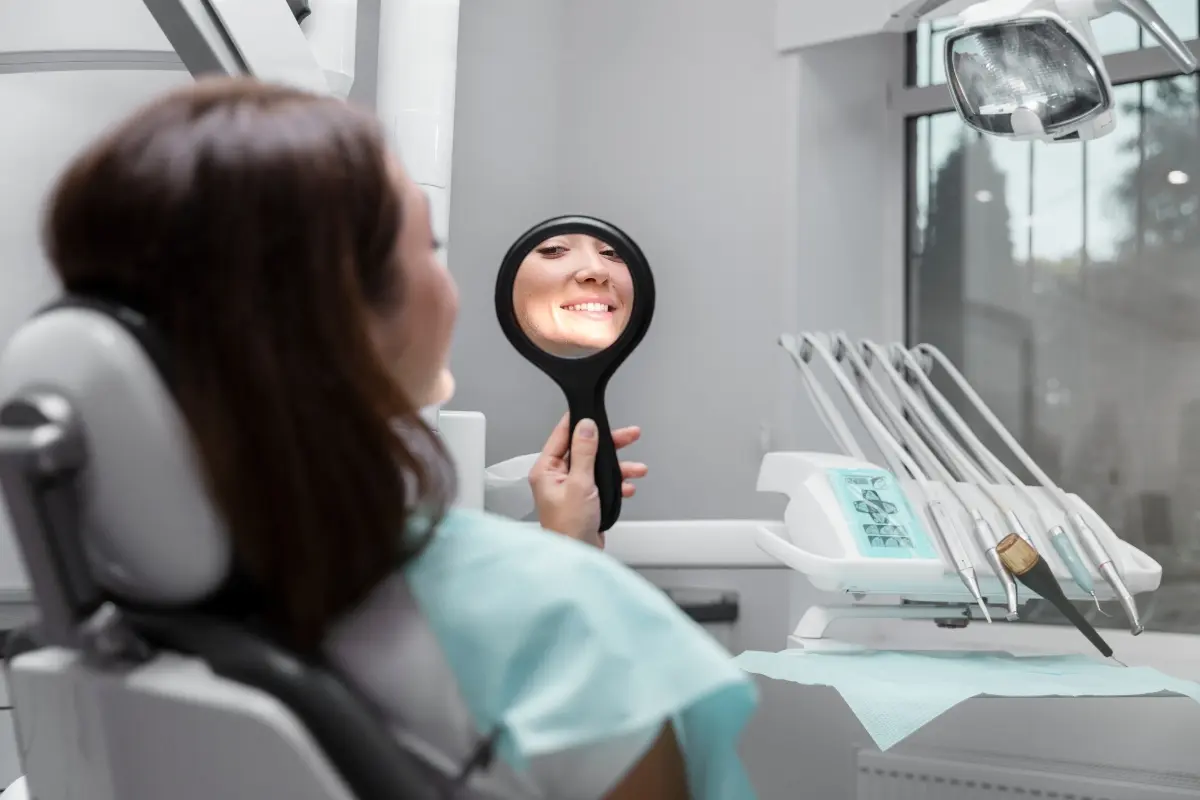Patient smiling in a dental chair holding a mirror at a modern dental clinic in Albania